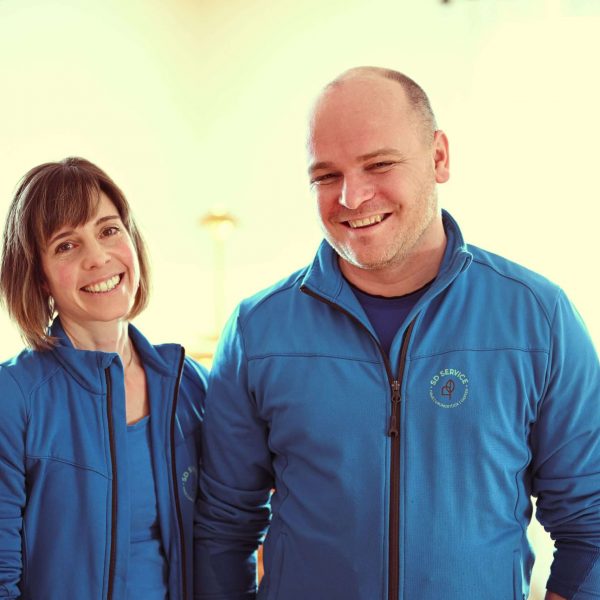 David und Simone Behnke in blauen SD Service Jacken. Beide sehen sympathisch aus und lächeln in die Kamera.