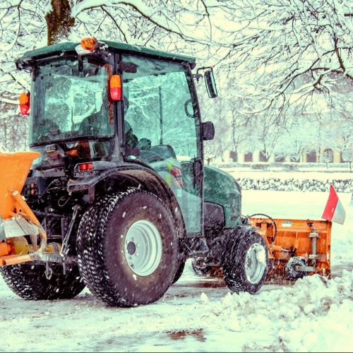 Ein Winterdienst Fahrzeug, in einem Schneebdeckten Stadtpark. Das Fahrzeug räumt den Weg frei von Schnee.